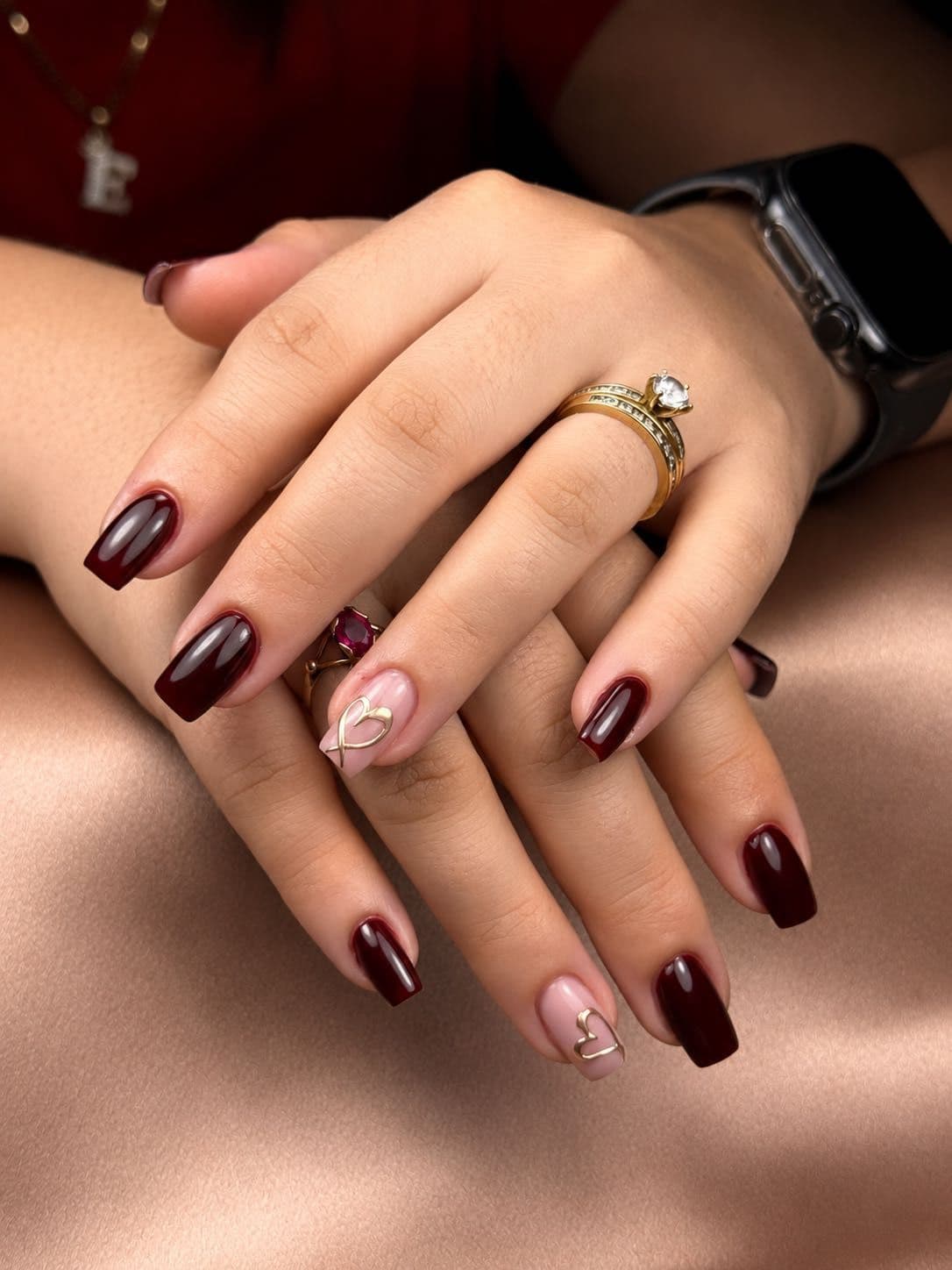 Burgundy nails with nude accents and raised gold hearts