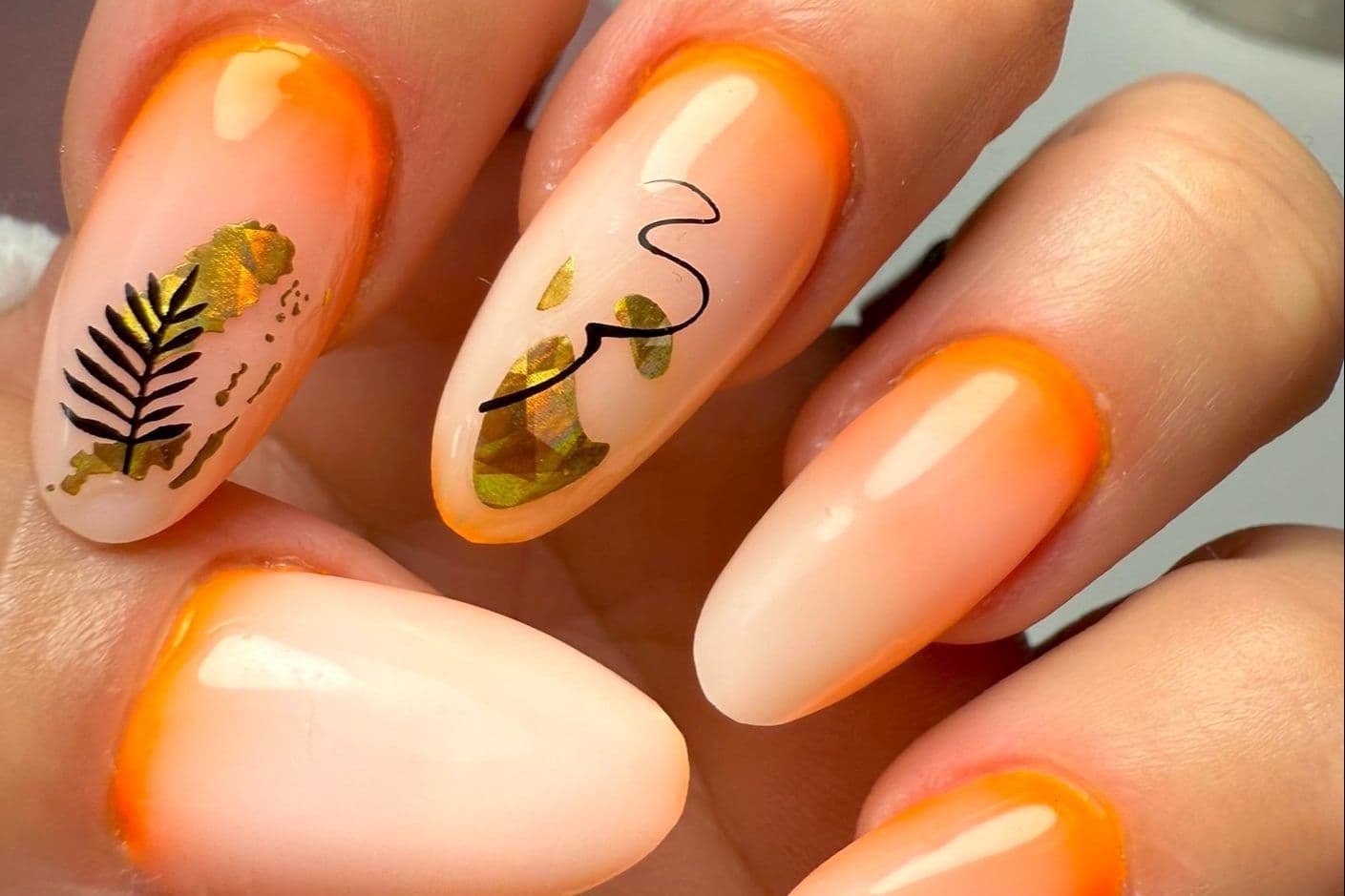 Almond nails with orange edges, nude centers, gold details and black lines