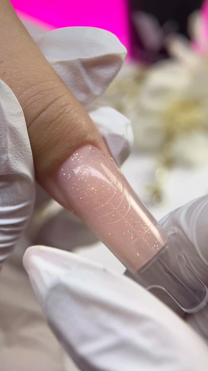 A nail built inside a clear form with glitter gel